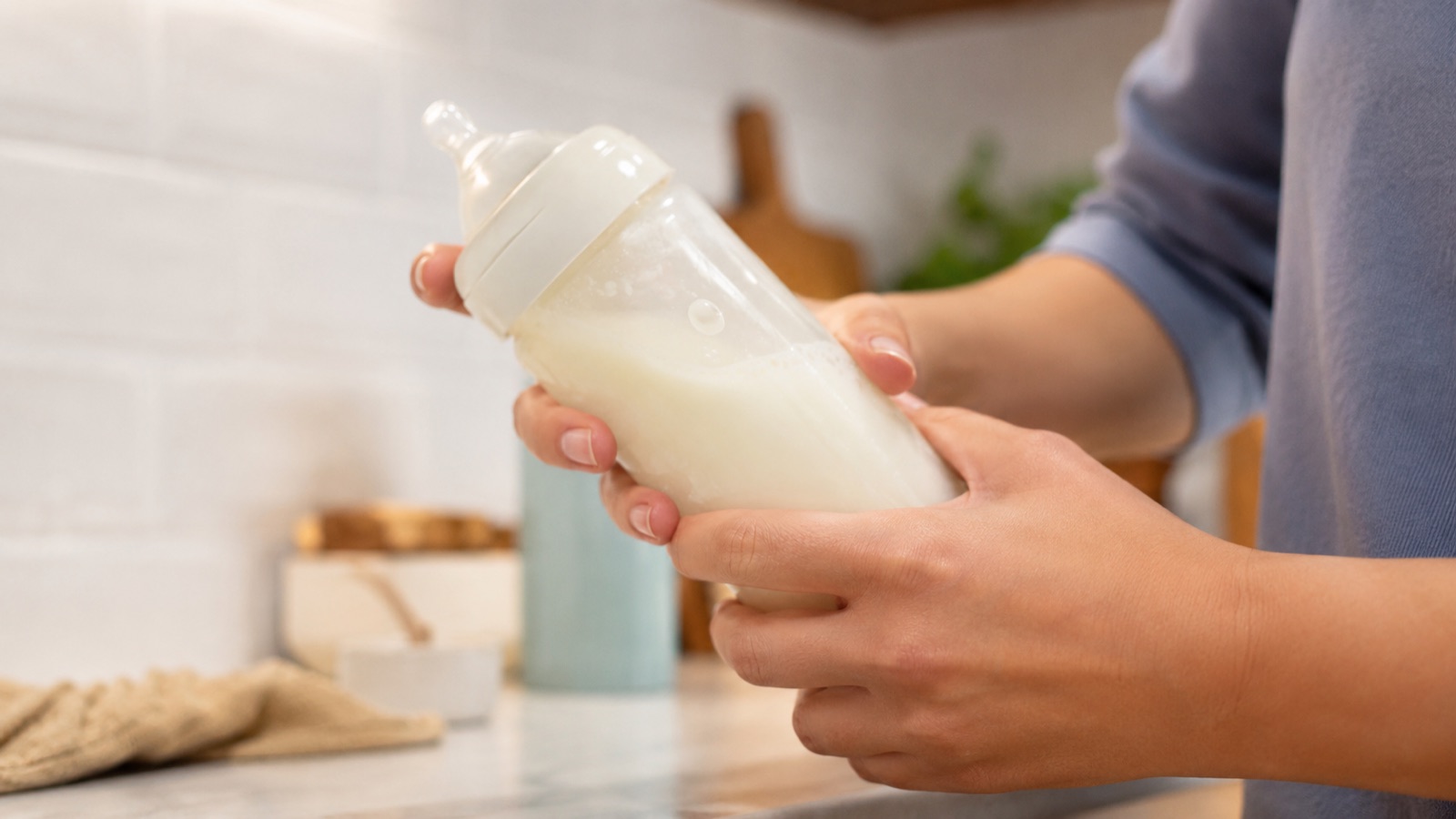 Twee handen scheppen melkpoeder met een maatschepje in een babyfles met water