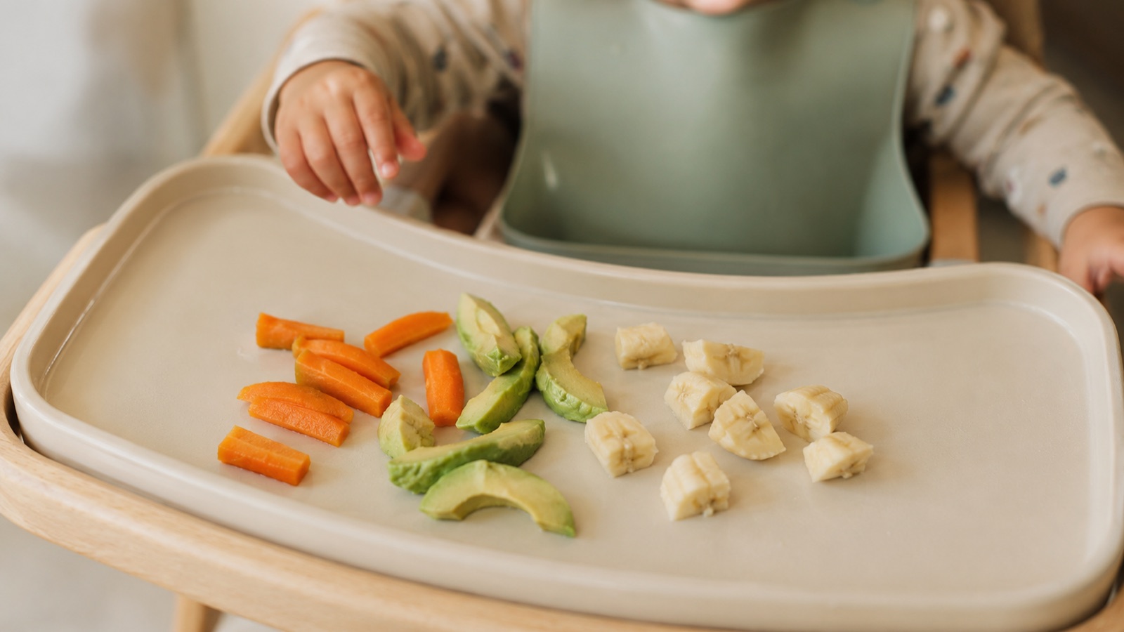Baby in een kinderstoel pakt zelf stukjes gekookte groente van het tafelblad